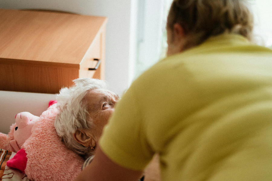 Opiekunka pochyla się na leżącą seniorką.